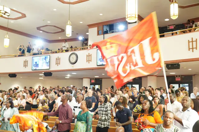 The congregation standing in worship, a “Jesus” flag raised above the pews